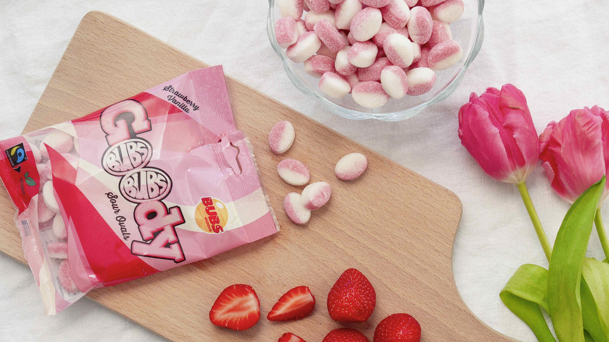 Opened bag of BUBS Goody Candy in Strawberry Vanilla flavor, surrounded by colorful gummy candies and fresh strawberries.